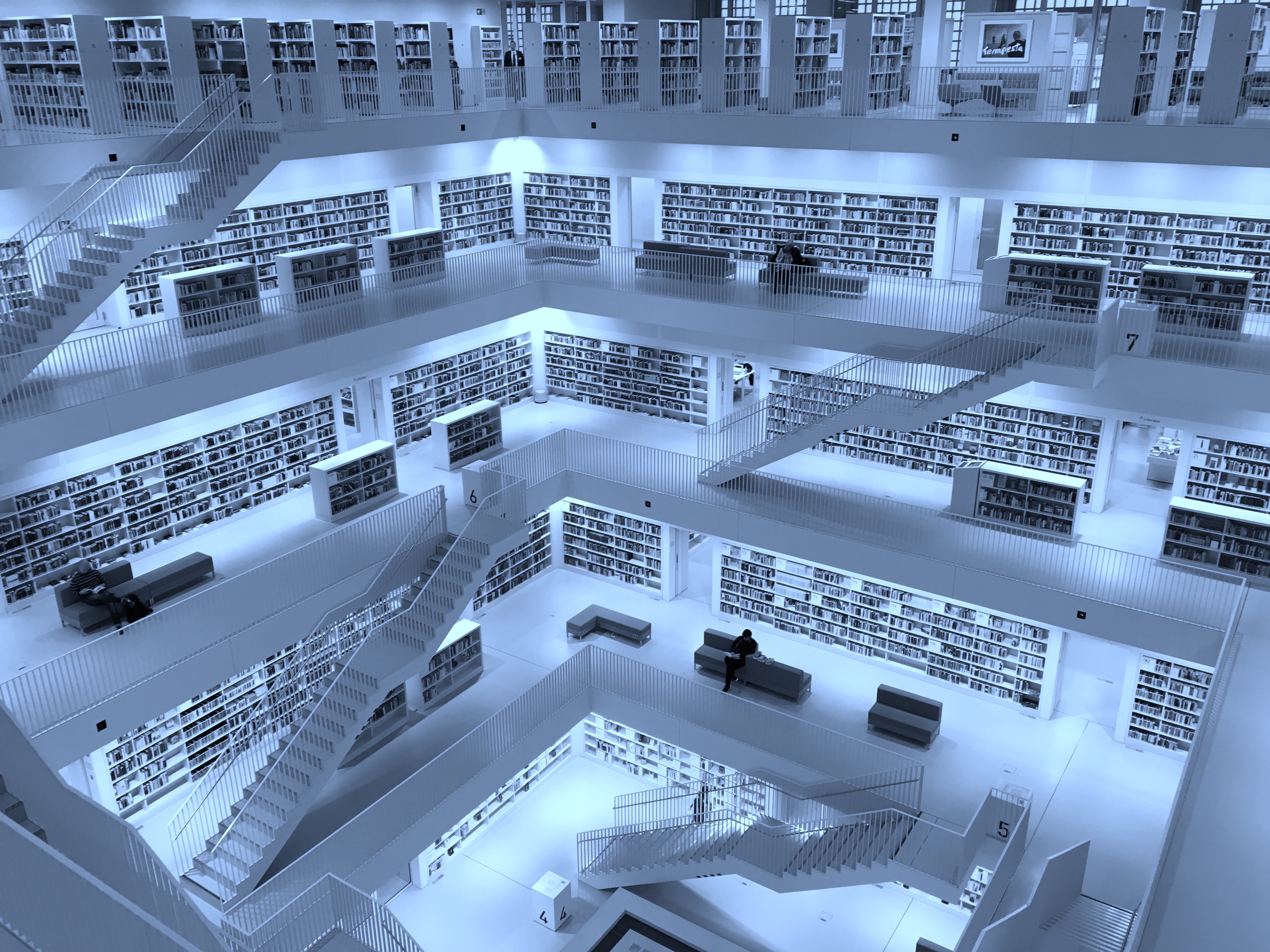 The inside of a geometric-looking library with many books and staircases cast in blue light