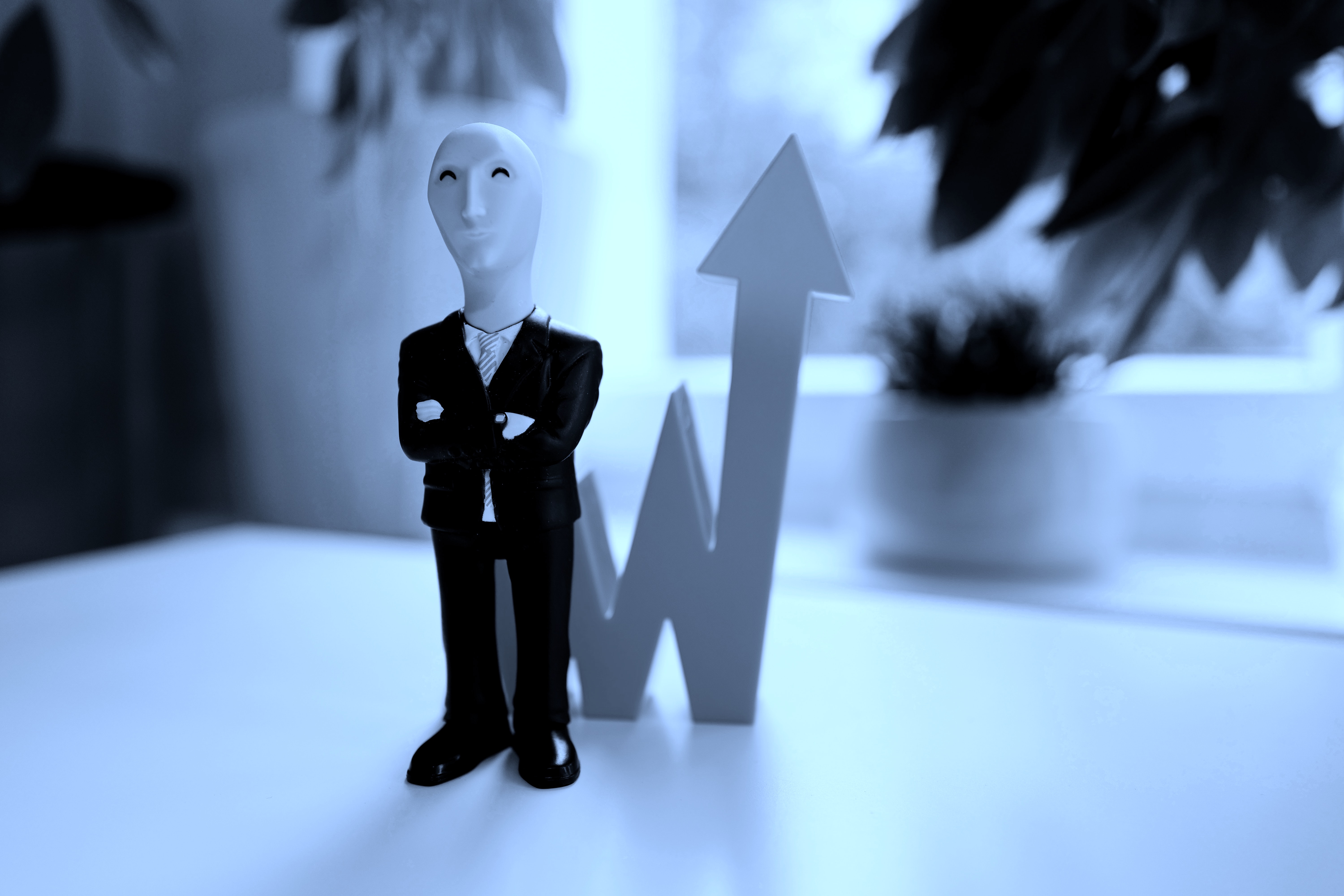 A vinyl figurine of the stonks meme -- a smiling man in a suit in front of an upwards arrow -- cast in blue light