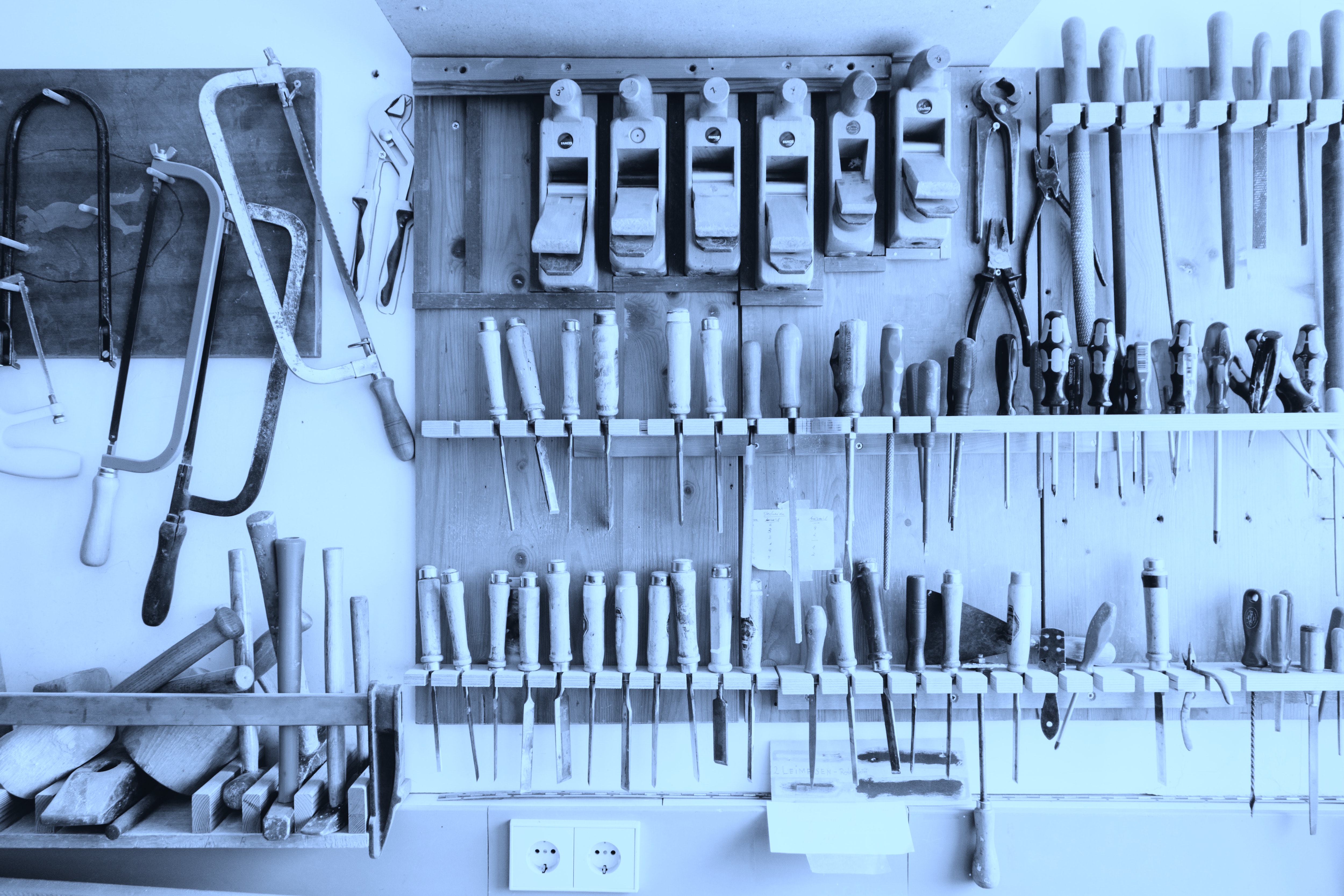 Saws and chisels hang on a wall cast in blue light